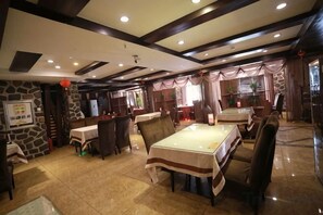 Ein Restaurant mit hoher Decke, Steinwänden und einem zentralen Esstisch, umgeben von Stühlen.