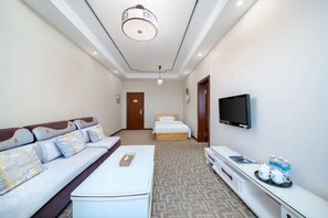 Habitación de hotel con sofá, cama, televisor, mesa de centro y minibar.