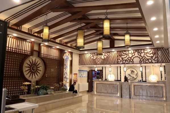 A hotel lobby with a reception desk, decorative wall panels, and hanging lanterns.