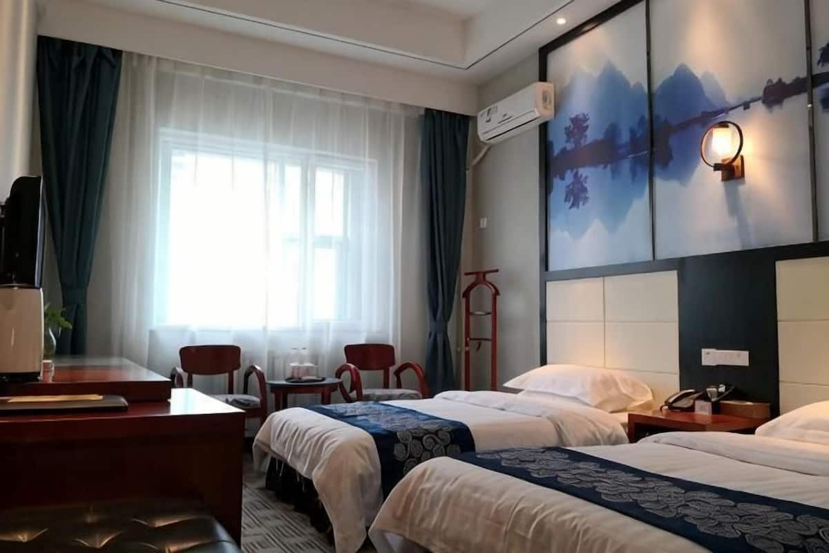 Habitación de hotel con dos camas, un escritorio con silla, una mesita pequeña y una ventana con cortinas.