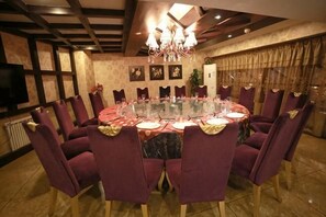 Une table de salle à manger ronde, entourée de chaises, un lustre au plafond et un téléviseur fixé au mur.