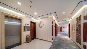 Un couloir d’hôtel avec un tapis à motifs floraux, des portes en bois et une horloge au mur.