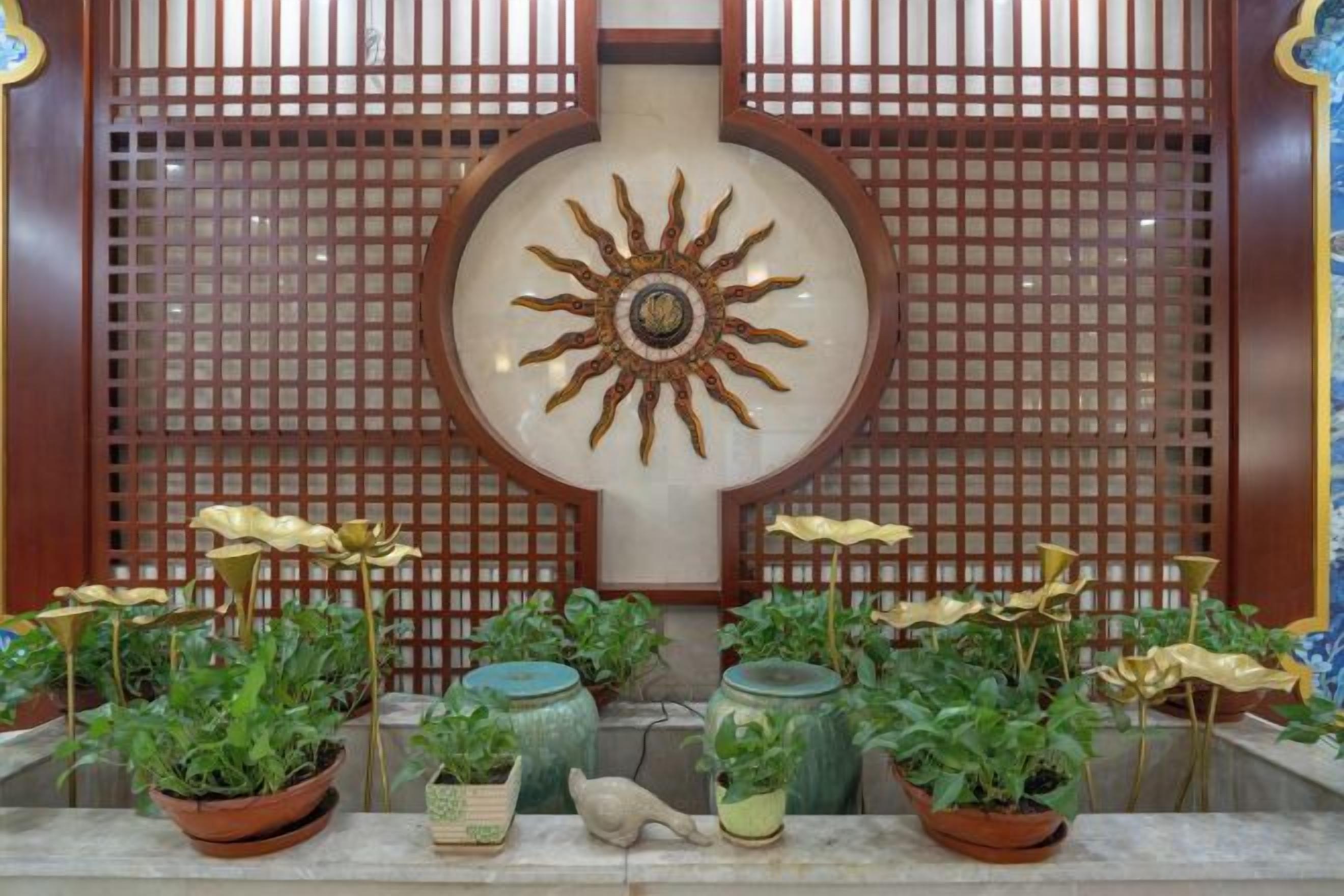 Una habitación tradicional con un panel de celosía de madera, un emblema decorativo de sol y plantas en macetas.