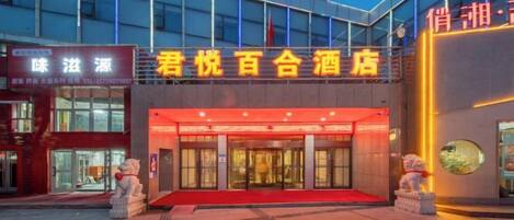 A hotel entrance with a red carpet, a large glass facade, and a signboard above the entrance.