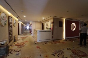 A hotel corridor with a reception desk, a decorative wall with a circular mirror, and a patterned carpet. - Junyue Baihe Theme Hotel (Karamay)