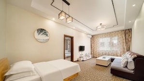 Une chambre d’hôtel avec un lit, un canapé, une télévision, une petite table et une fenêtre avec des rideaux.