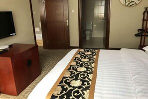 Habitación de hotel con una cama, un aparador de madera, un televisor y una puerta corredera que da a un baño.