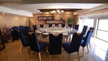 A dining area with a round table set for six, surrounded by blue chairs, in a room with a patterned wall and a ceiling light fixture.