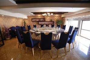 Un comedor con una mesa redonda dispuesta para seis personas, rodeada de sillas azules, en una habitación con pared estampada y una lámpara de techo.