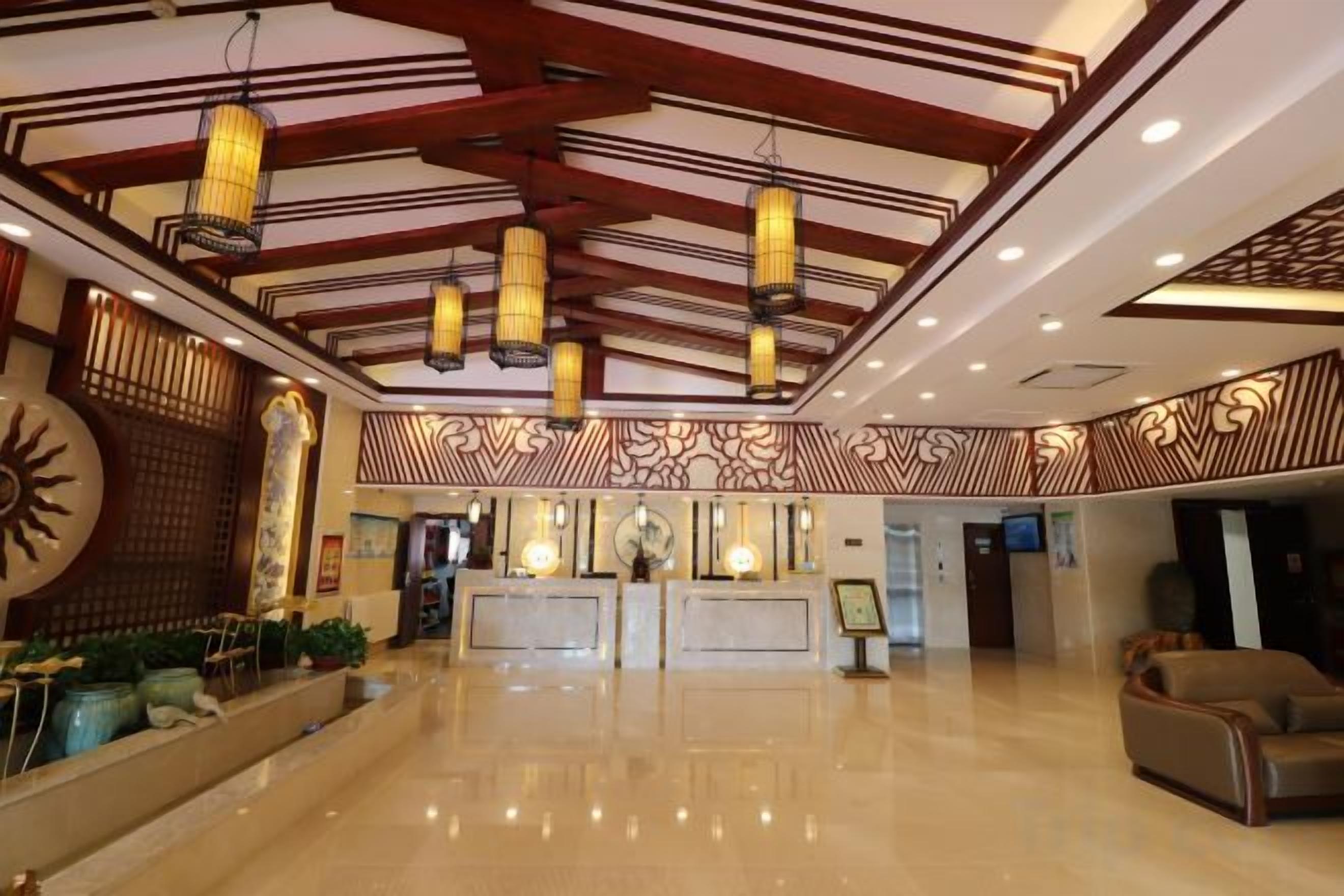 Een hotellobby met een receptiebalie, een zithoek en een decoratief plafond.