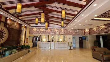Een hotellobby met een receptiebalie, een zithoek en een decoratief plafond.