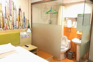 Habitación de hotel con cama, mesita de noche pequeña, y baño que incluye inodoro, lavabo y espejo.