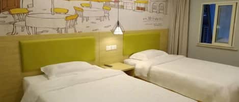 A hotel room with two beds, a small table, a lamp, and a wall mural.