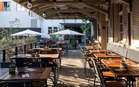An outdoor dining area with wooden tables and chairs, umbrellas, and hanging light fixtures.