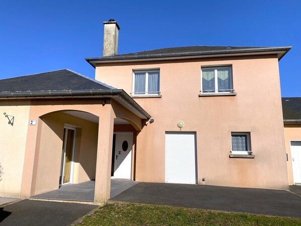 Un bâtiment à deux étages, doté d’une façade beige, d’une cheminée et d’une porte de garage.