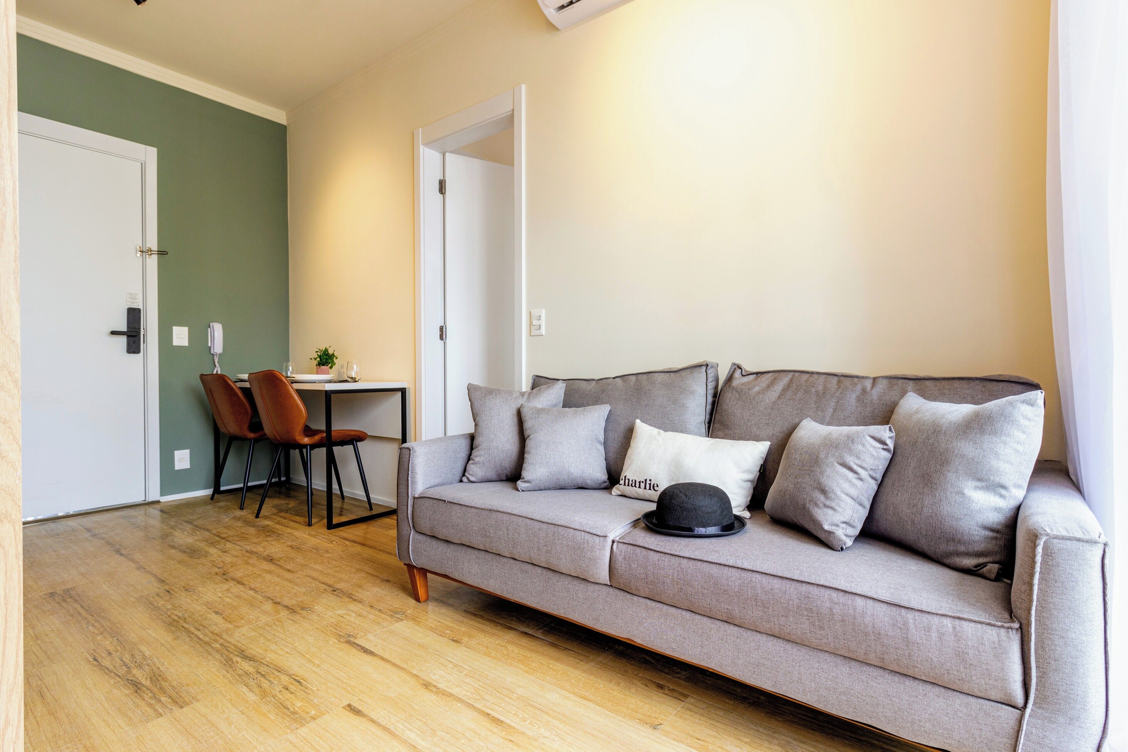 A living room with a grey sofa, a dining table with chairs, and a door leading to another room.