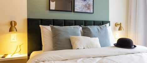 A neatly made bed with a dark headboard, white bedding, and a black hat on the pillow. There are two framed pictures on the wall above the bed.
