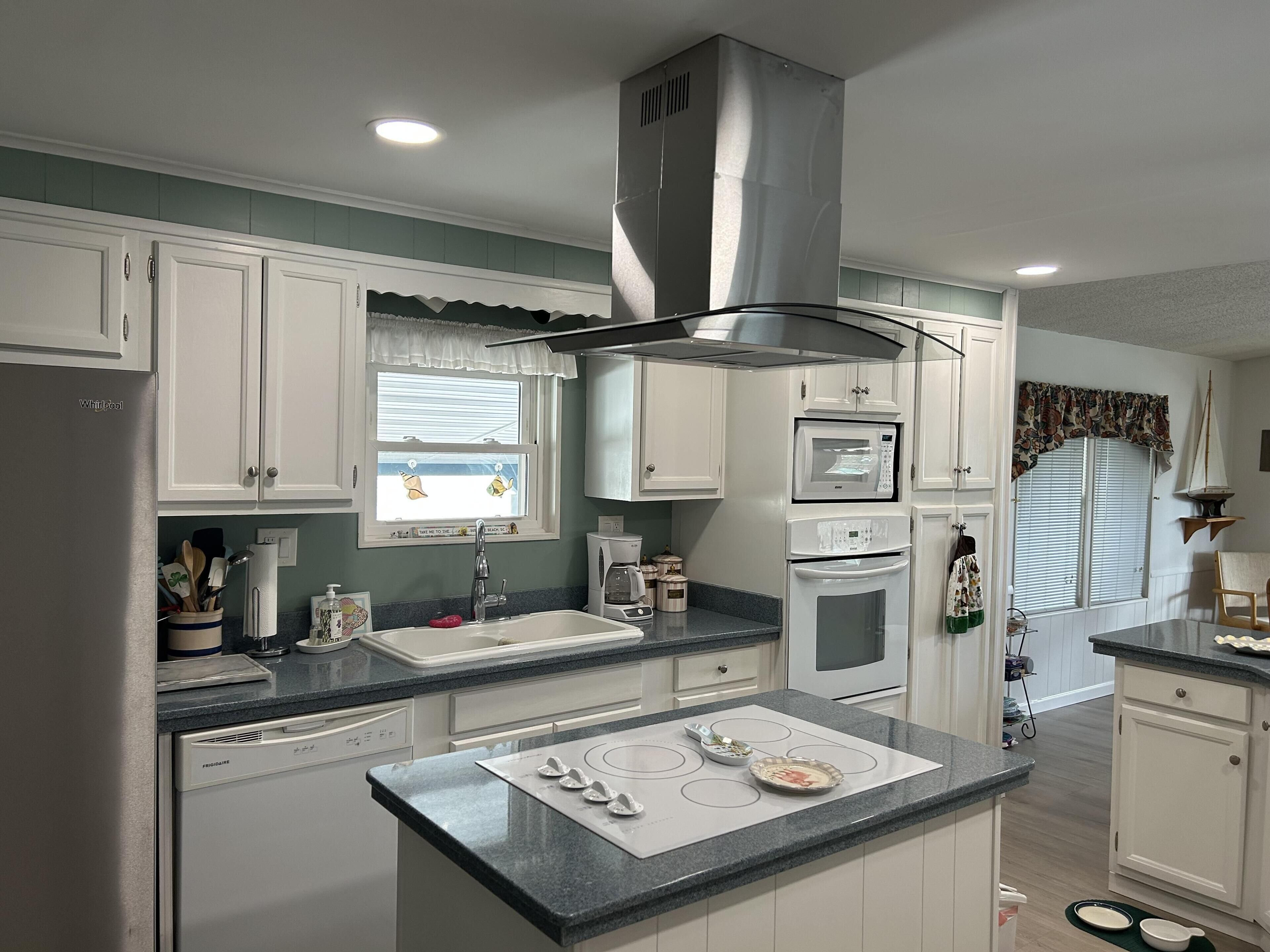 A modern kitchen with white cabinets, a stainless steel range hood, a built-in microwave, and a dishwasher.