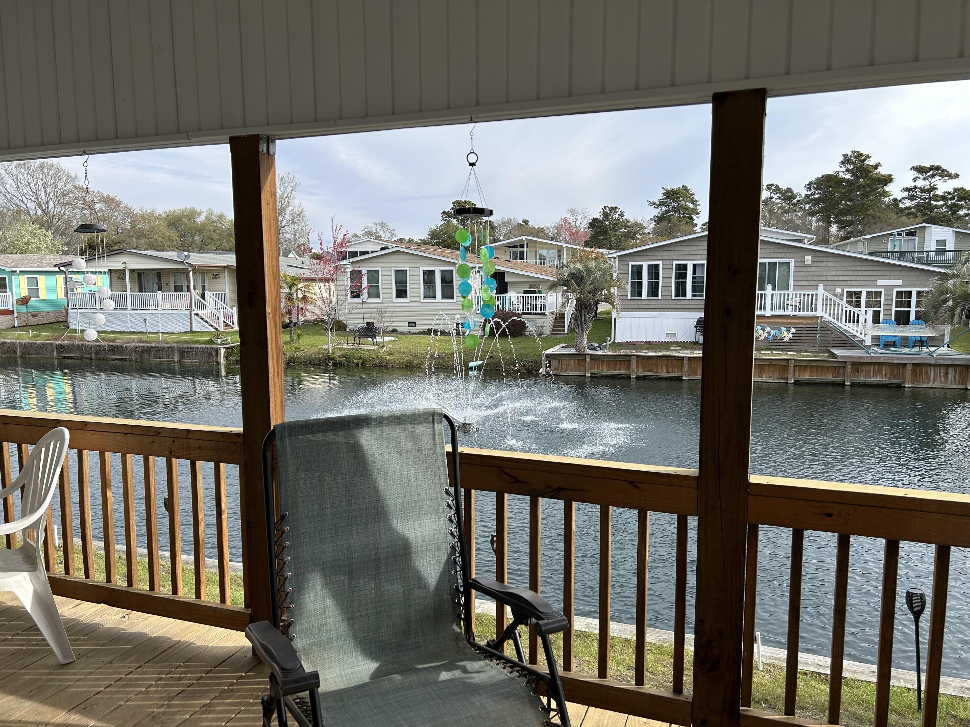 A covered deck with a view of a lake, houses, and a fountain.