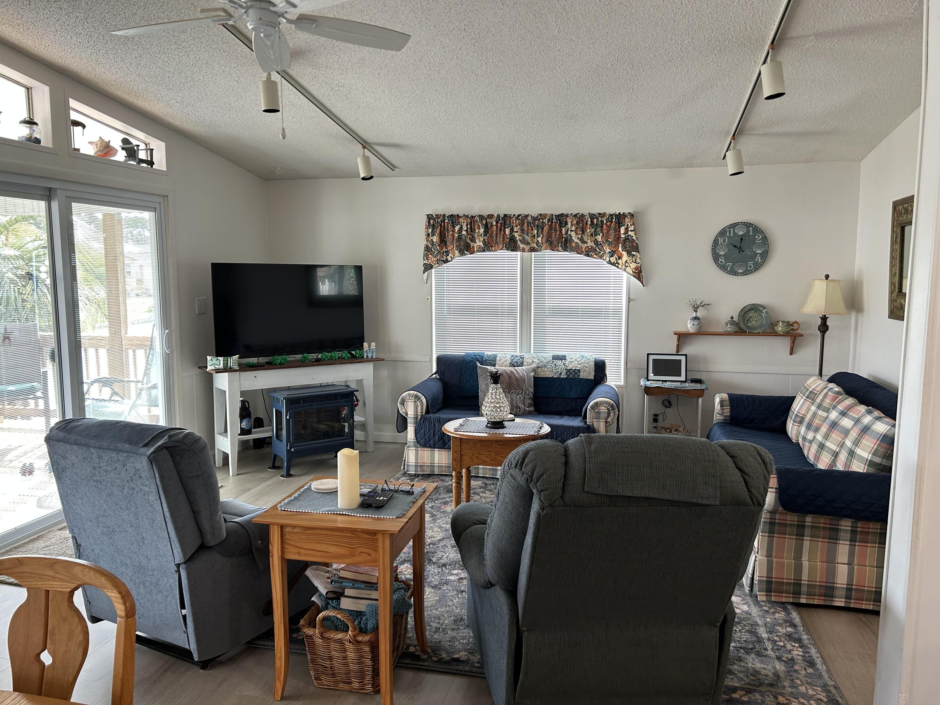 A living room with a television, sofas, a fireplace, and a ceiling fan.