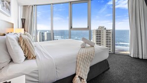 Habitación de hotel con una cama grande, vista al océano y un paisaje urbano al fondo.
