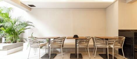 A modern dining area with a rectangular table and four wicker chairs, a potted plant, and a fireplace.