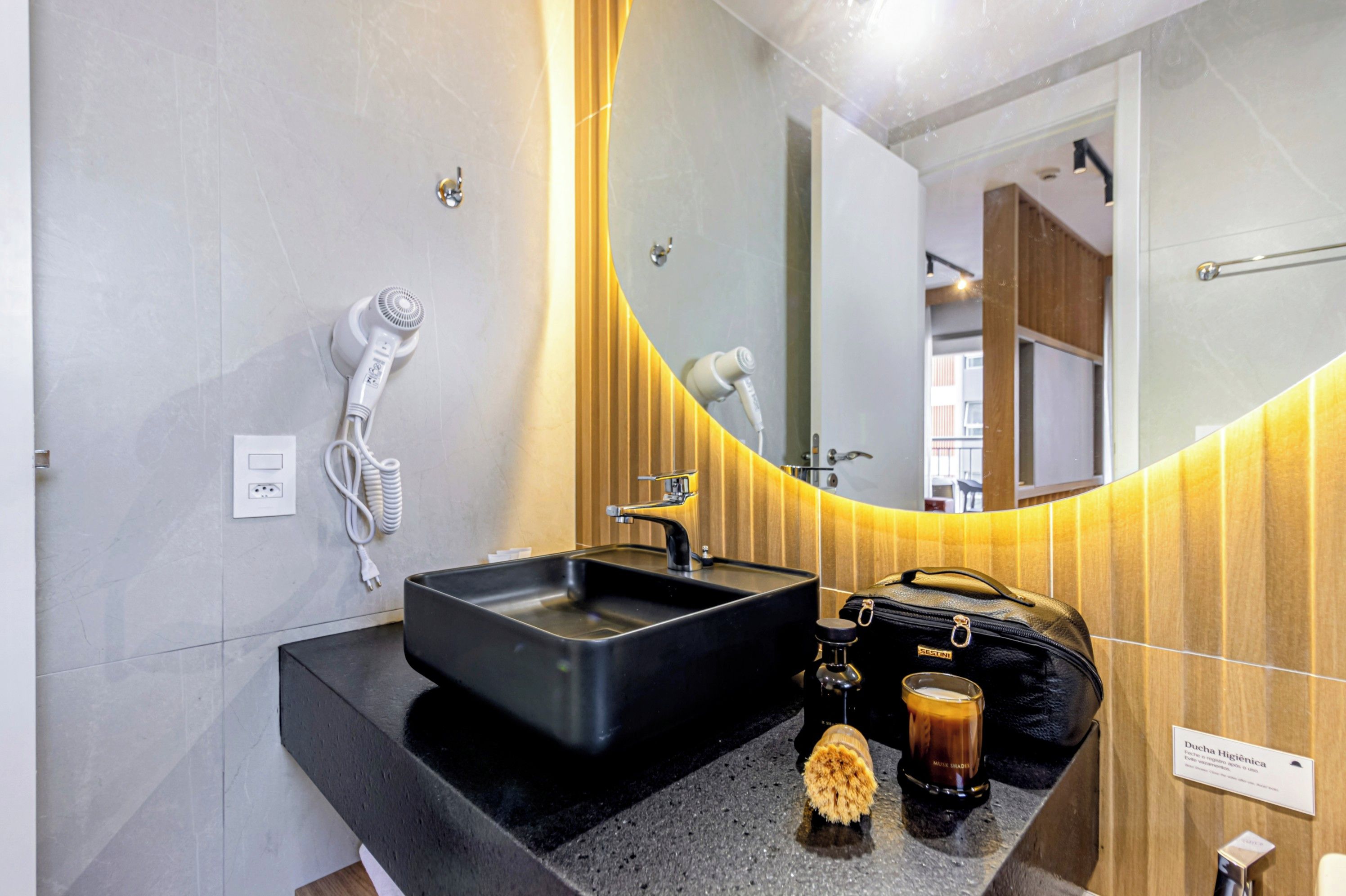 Un baño moderno con un lavamanos negro, un secador de pelo y un espejo.