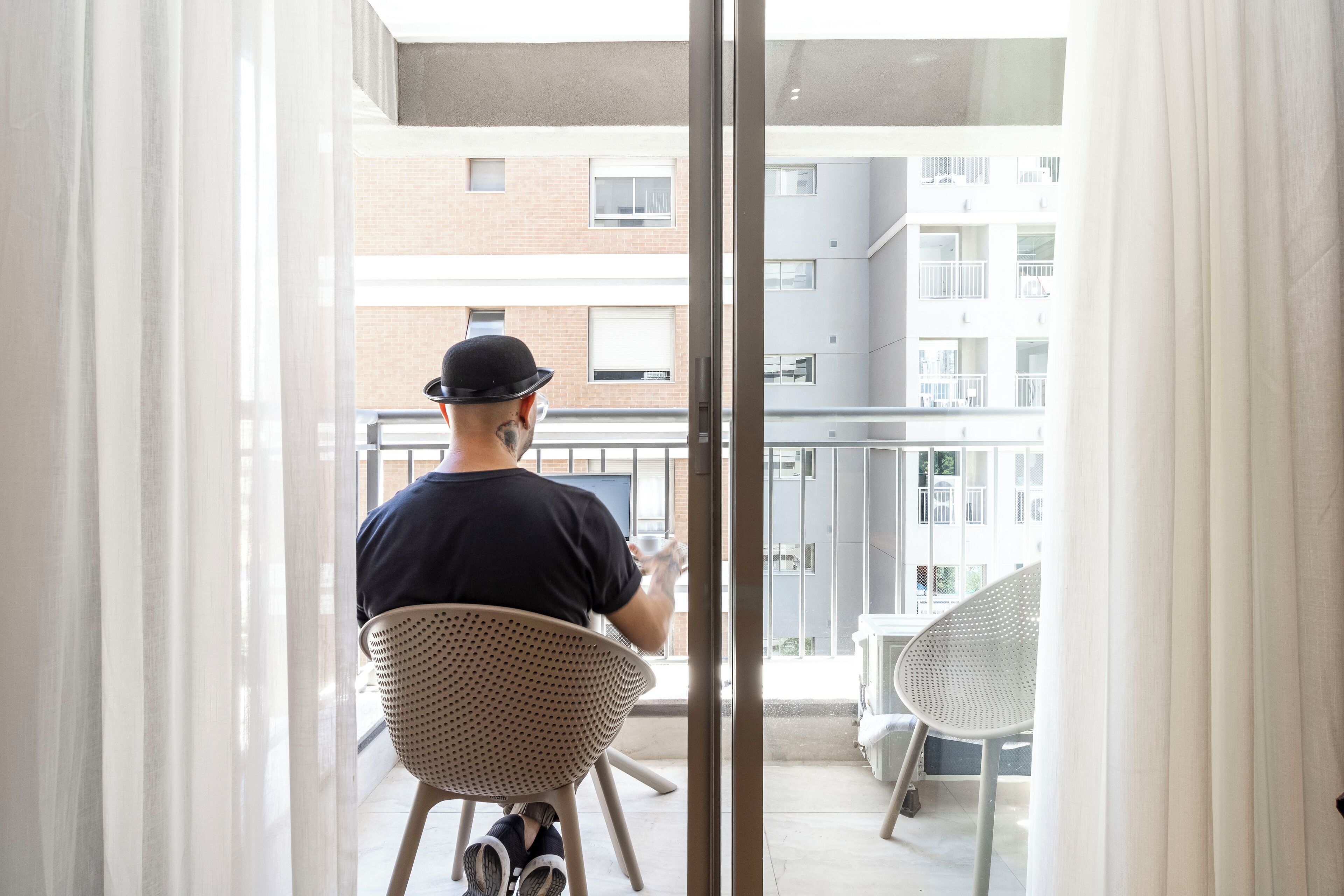 Mies istuu rottingista tehdyssä tuolissa parvekkeella, jolta on näkymä rakennukseen.