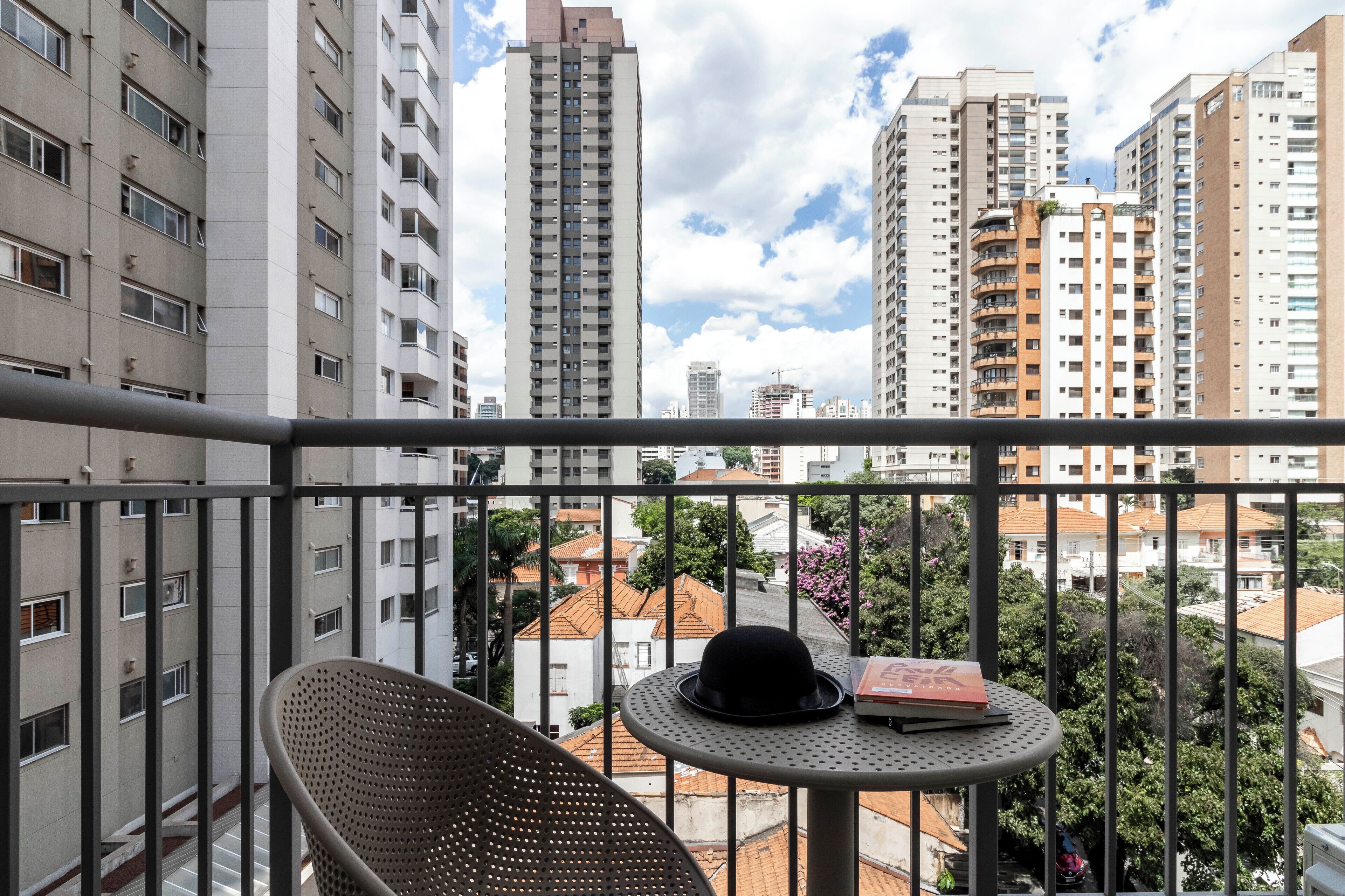 Un balcón con una silla y una mesa, con vistas a un paisaje urbano con edificios altos y árboles.