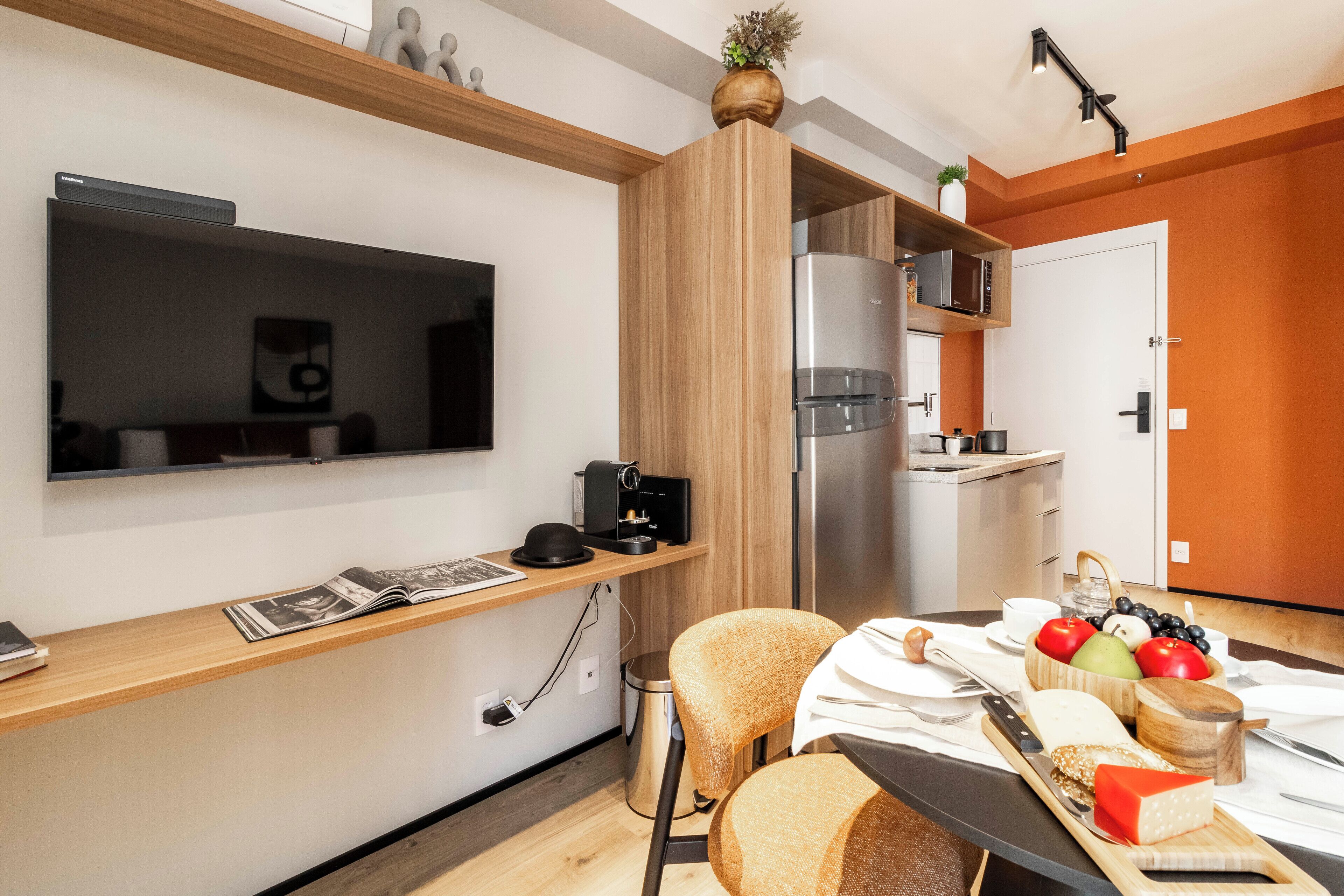 A compact kitchen with a microwave, refrigerator, and wooden shelves.