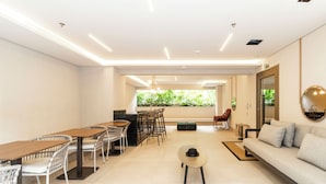 A modern, well-lit dining area with wooden tables and white chairs, a sofa, and a large mirror.