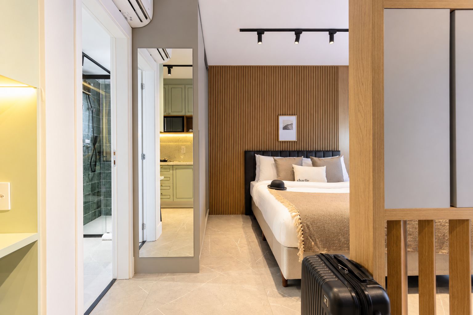 Ein modernes Hotelzimmer mit Bett, Koffer, einer Wand aus Holzpaneelen und Blick zur Küche.