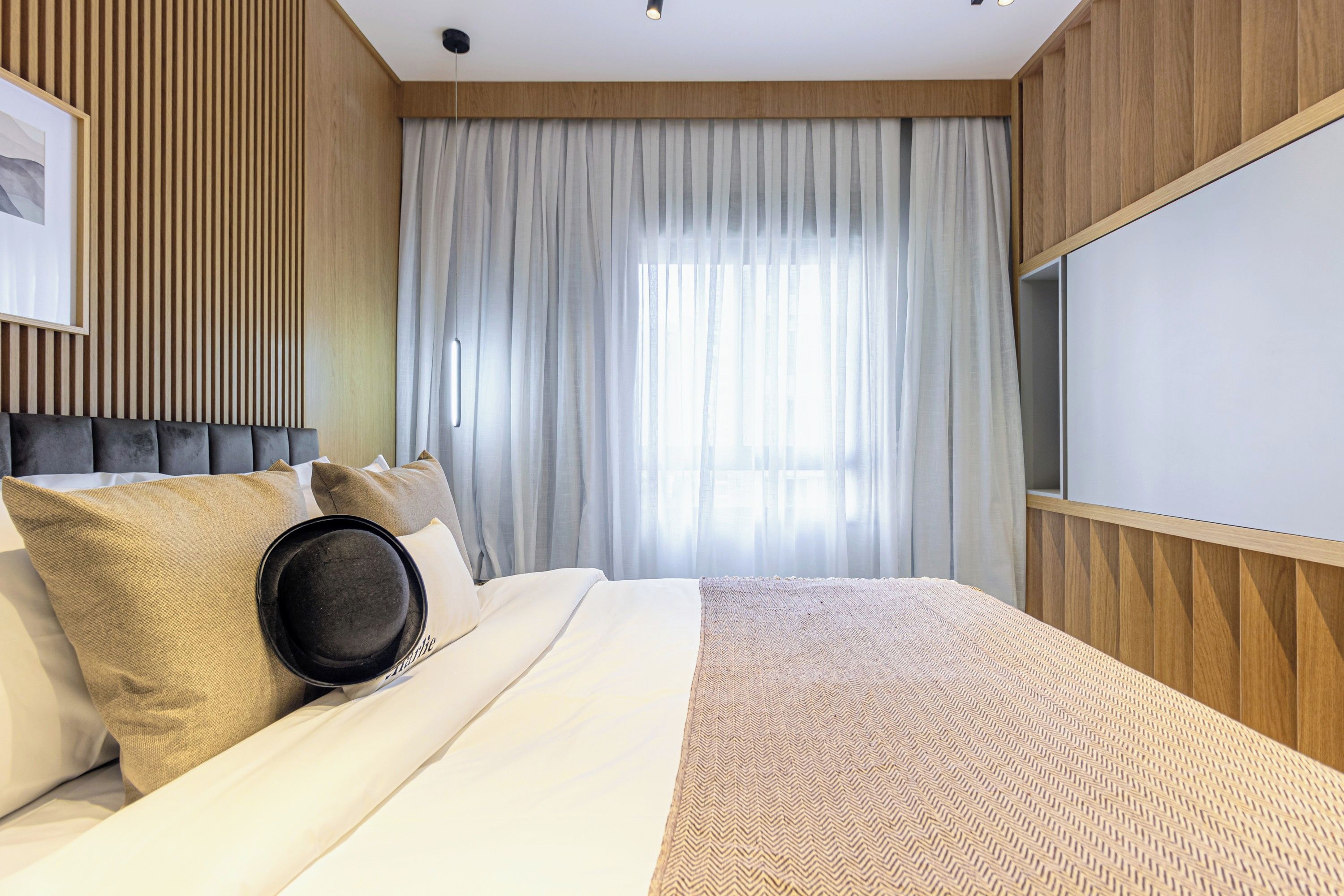 Habitación de hotel con cama, televisor de pantalla plana y un amplio ventanal con cortinas.