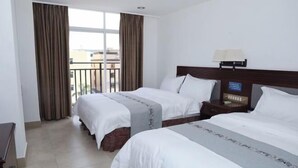 A hotel room with two beds, a nightstand with a lamp, and a view of the outside through large windows. - Haixuan Hotel (Taishan)