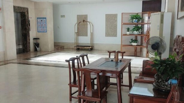A spacious lobby with a wooden dining table and chairs, a fan, and a plant. - Haixuan Hotel (Taishan)