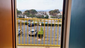 Vista desde un balcón con barandilla amarilla, sobre un estacionamiento con varios coches y un paisaje urbano distante con montañas.