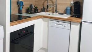 Una cocina compacta con armarios blancos, lavavajillas Bosch, horno integrado, pileta con grifo moderno y cafetera.