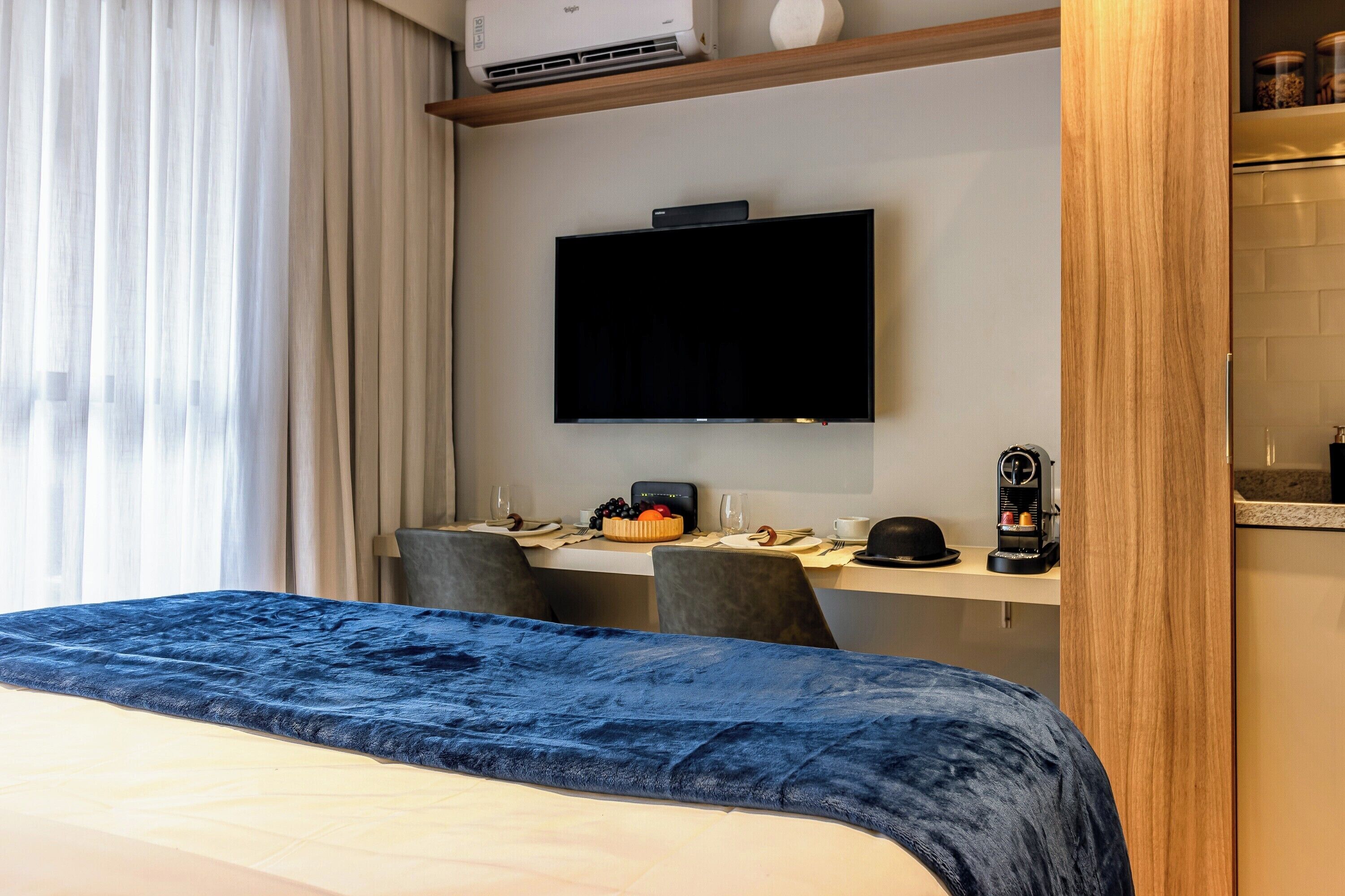 Ein Hotelzimmer mit Bett, Schreibtisch, Flachbildfernseher, Kaffeemaschine sowie Essbereich mit Stühlen und Tisch.