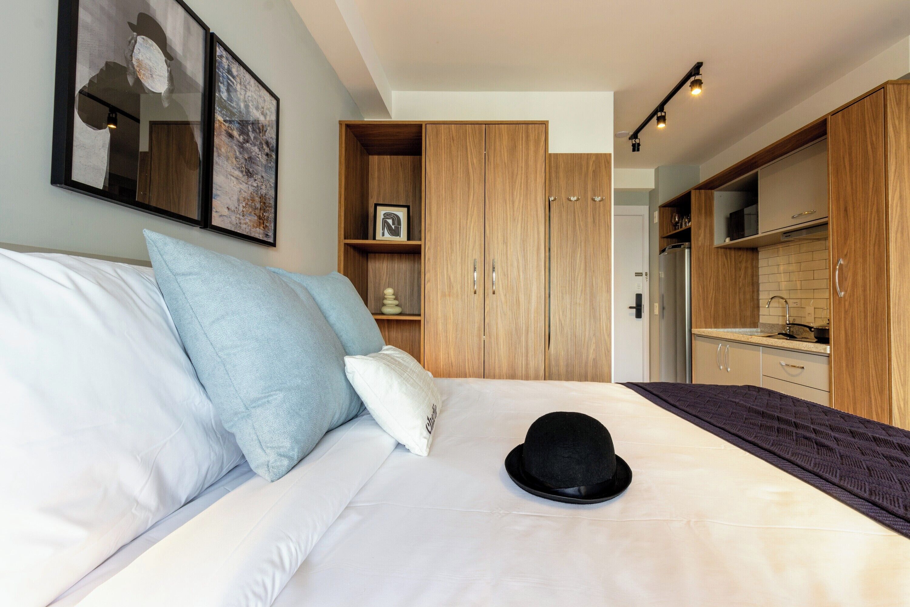 Une chambre à coucher avec un lit, des oreillers, un chapeau, une armoire et un coin cuisine.