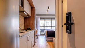 A narrow hallway with a kitchenette on one side, a bed with a view to the outside, and a door with a 'BLOCK' sign. - Charlie  Lumiere Klabin (São Paulo)