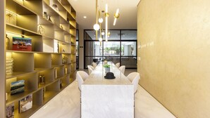 A modern dining area with a marble table, white chairs, and a long bookshelf with various items. - Charlie  Lumiere Klabin (São Paulo)