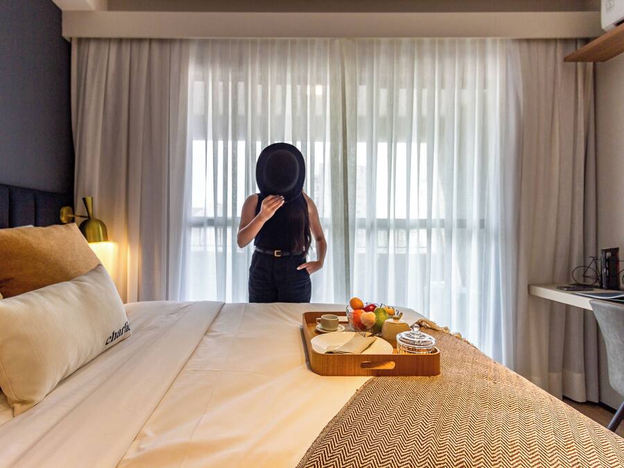 Quarto de hotel com cama, bandeja de café da manhã e janela com cortinas.