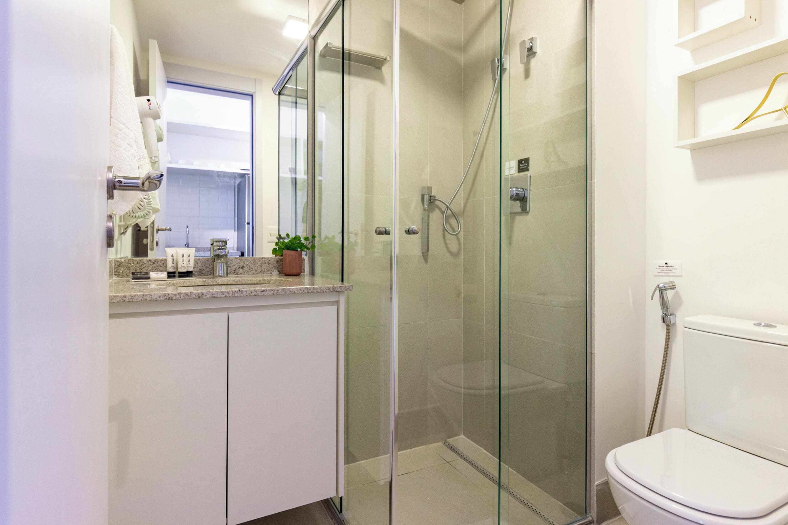Ein modernes Badezimmer mit einer in Glas eingefassten Dusche, einer weißen Toilette und einem Waschtisch mit Pflegeprodukten.