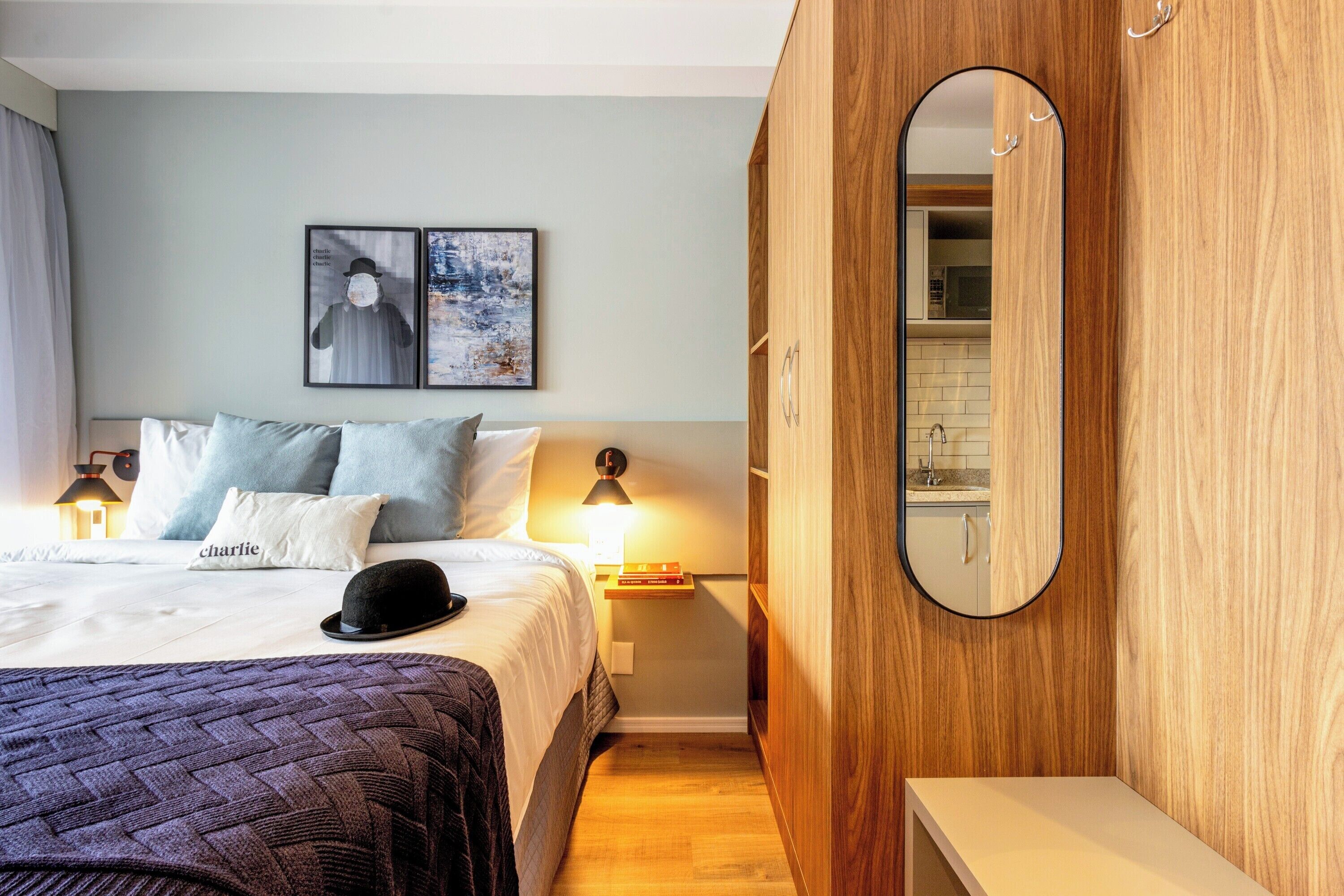 A neatly arranged bedroom with a bed, bedside lamps, a nightstand, a mirror, and a wall-mounted artwork.