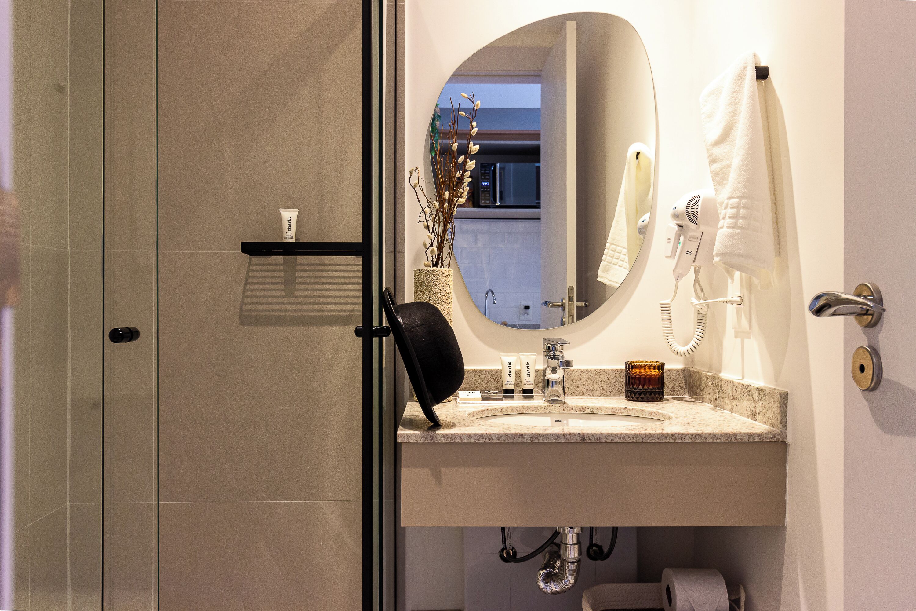 A bathroom with a glass shower door, a sink with a vanity mirror, a hairdryer, and a towel hanging on the wall.