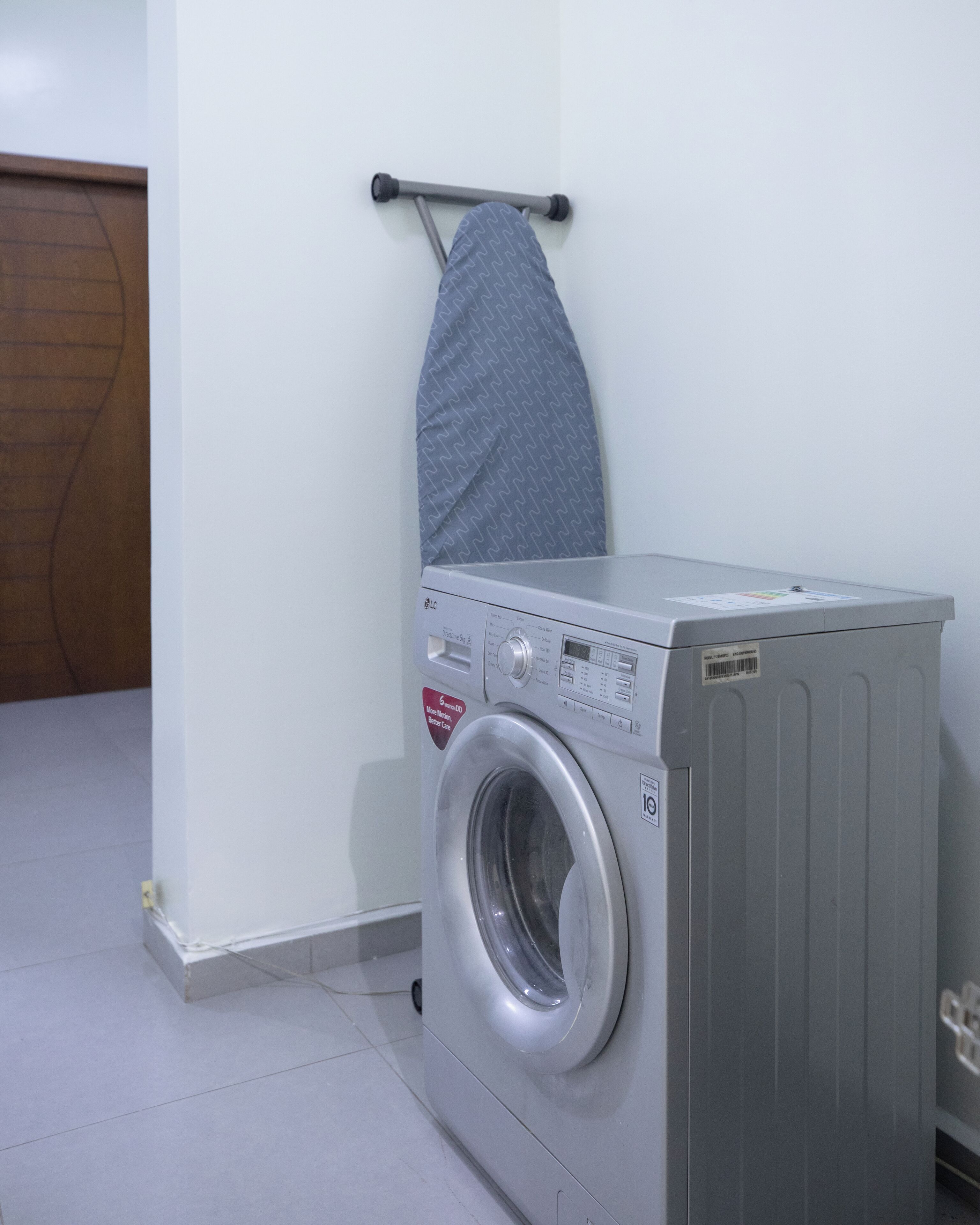 A front-loading washing machine in a room with white walls and a tiled floor.
