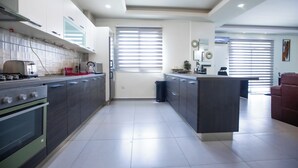 A modern kitchen with a central island, built-in oven, and a dining area with a red chair. - TCC APARTMENT (Accra)