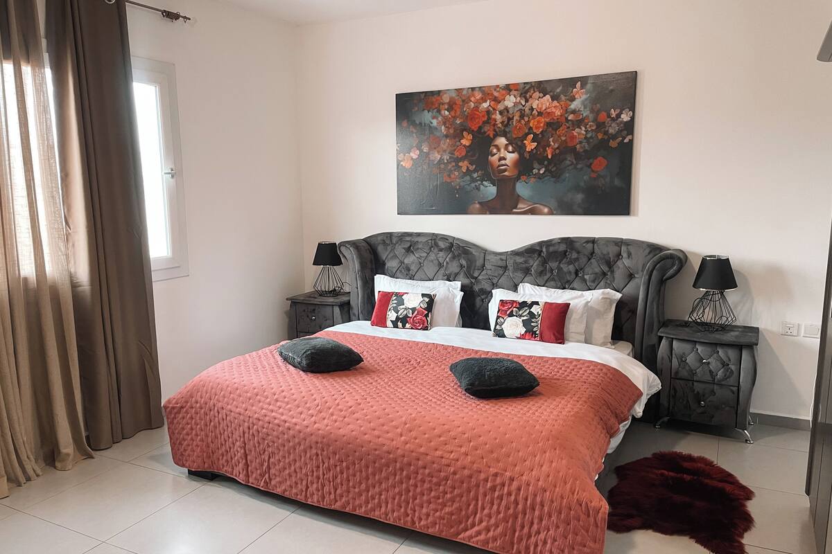 A bedroom with a large bed, two bedside tables with lamps, a painting on the wall, and a window with curtains.