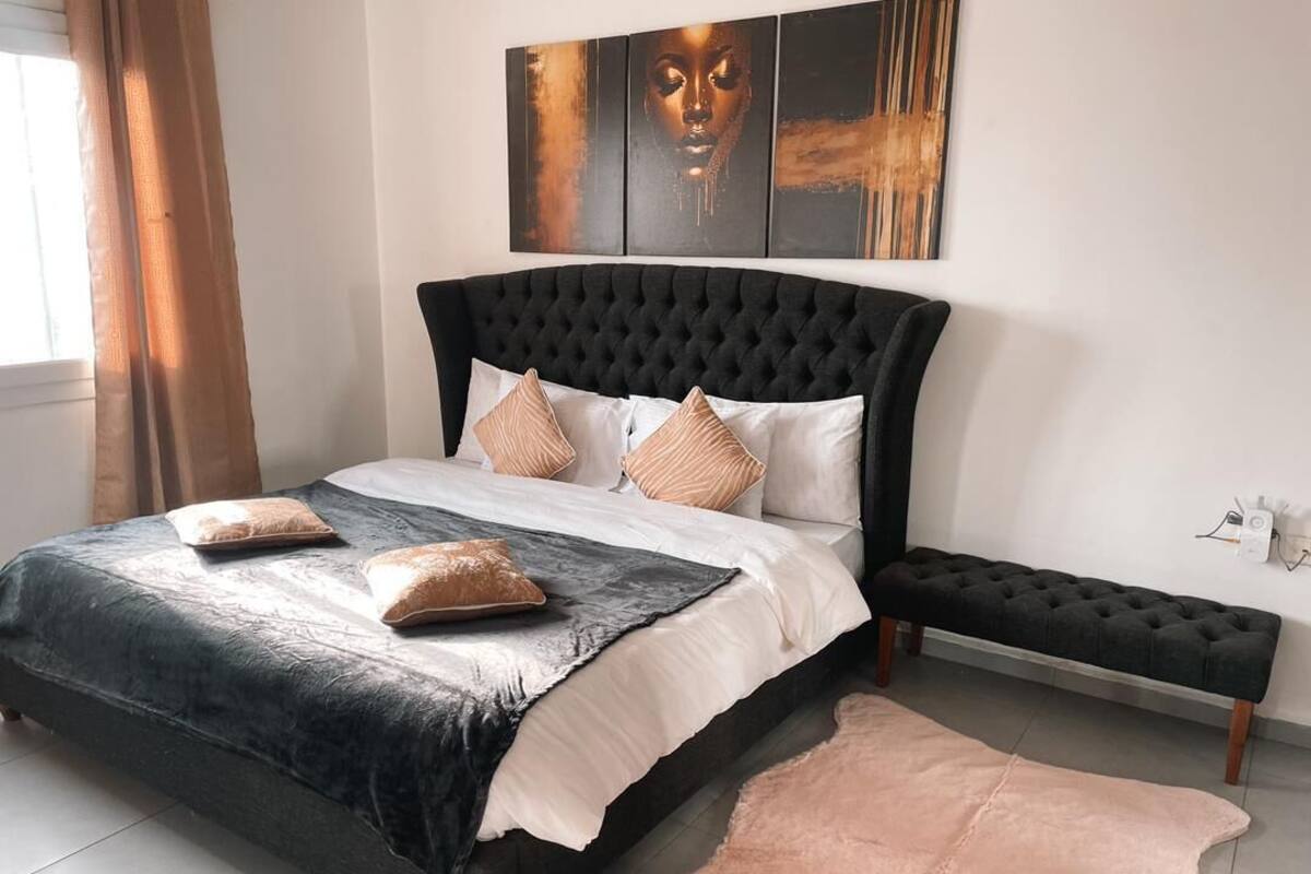 A bedroom with a tufted headboard, a large bed with two pillows, a bench, and a rug.