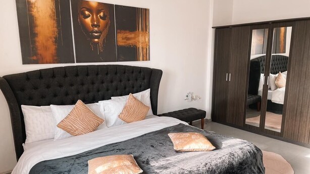 A bedroom with a large bed, a dark headboard, and a wardrobe with a mirror. - TCC APARTMENT (Accra)